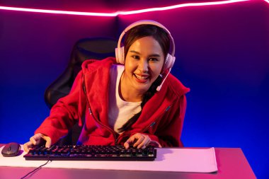İnternet üzerinden kulaklık takıp gülümseyen Asyalı güzel kız flamasının sunucu kanalı izleyicilerle internet üzerinden konuşma yapıyor. Esport yetenekli takım oyuncuları neon mavi odada. Taktik.