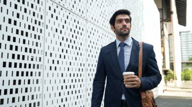 Elinde kahve fincanı tutarken takım elbise içinde yürüyen yetenekli bir iş adamı. Mimari binanın yanında duran profesyonel yönetici. Sabahları işe gidiyorum, başarılı bir iş arıyorum. Sevinçli..