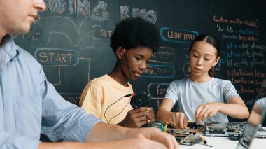 Genç öğrenci BTMM sınıfında öğretmenlik yaparken denetleyiciyi tamir ediyor. Akıllı kız elektronik alet ve karatahta kullanırken eğitmen el bilgisayarı. Öğretim.