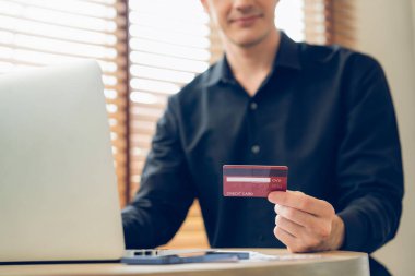 Genç adam internet bankacılığı için kredi kartlı dizüstü bilgisayar kullanıyor. İnternet üzerinden alışveriş yapıyor. Banka kartıyla modern ve kullanışlı online satın alma. Açılıyor