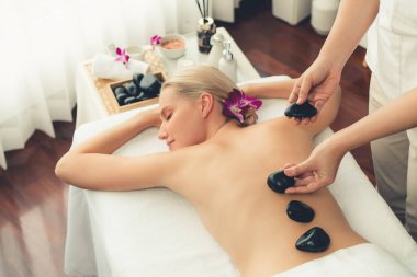 Lüks tatil köyündeki kaplıcalarda sıcak taş masajı. Gün ışığı sükunet ortamında, mutlu kadın müşteri bazalt taş masajından zevk alıyor. Rahatlatıcı bir sıcaklıkla vücudun üzerinde süzülüyor. Sessiz.