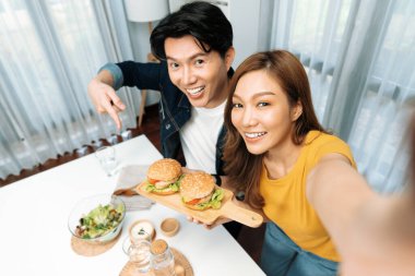 Gülümseyen ev sahibi aşçıların akıllı telefonuyla fotoğraf çekerken üst görüntüsü yemek programında çift hamburger tutarken sosyal medya kanalında ev yapımı salata tabağıyla kolaylıkla görülebiliyor. İnfobahn.