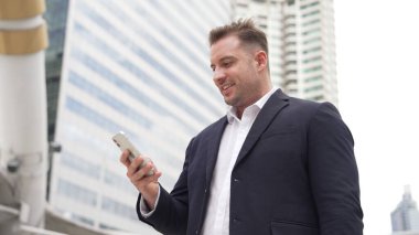 Kafkasyalı iş adamı şehir merkezinde dururken cep telefonlarını kontrol ediyor ve pazarlama ekibinden satış raporlarını inceliyor. Yetenekli bir yönetici cep telefonu üzerinde çalışıyor ve veri analizine bakıyor. Urbane.