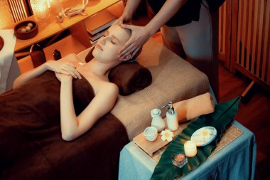 Beyaz kadın stres önleyici kafa masajı yapmaktan ve lüks otel veya otelde sıcak mum ışığında yüz güzelliği eğlencesi yapmaktan zevk alıyor. Sessiz.