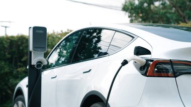 Doğal yeşil şehir parkındaki otoparkta EV elektrikli araba şarj pili. Sürdürülebilir ve çevre dostu şehir yolculuğu için yenilenebilir otomobil için alternatif temiz enerji teknolojisi. Eşzamanlama