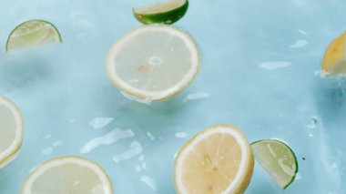 Dilimlenmiş limon makrosu, limon ve limonla suya dökülüyor. Mavi arka planda yüzüyor. Citrus meyve hareketi berrak suda ilerliyor. Citrus tazeliği. Tazelik ve susuzluk kavramı. Pabulum.