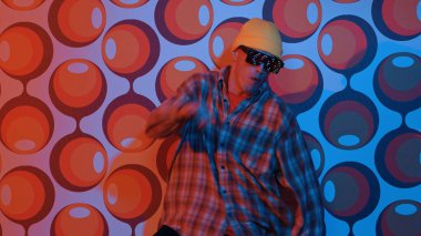 Profesyonel break dansçı, parti sahnesinde balon arka planlı gözlük takıyor. Havalı giyinen yetenekli bir sanatçı enerjik hareketler ve ayak sesleri göstererek müziğe yöneliyor. Mutluluk.