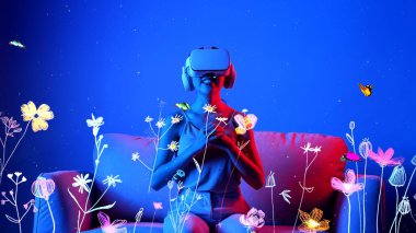 Kanepede oturmuş, VR 'ı açıp metatif etkileşimli sanal neon çiçeğini üç boyutlu polen grafik meta bahçe dünyası ile kırmızı ışıkta yeni bir kelebek çiçeğine çeviriyor. Halüsinasyon.