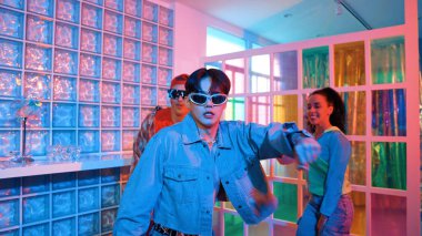 Asyalı adam gece kulübünde çeşitli neon ışıklarda dans ederken kolunu oynatıyor. Modern kulüpte çok kültürlü hippilerle dans eden şık elbiseli mutlu dansçı. Mutluluk.