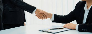 Yönetim kurulunda iki yönetici el sıkışıyor, iki şirketi birbirine bağlıyor. El sıkışmak iş ortaklığını ve işbirliğini simgeler. Şirket kazancı ve birleşme konsepti. Kurnaz.