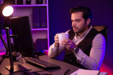 Gülümseyen zeki işadamı, elinde kahve fincanı olan satış ekibiyle buluşuyor ve geceleri Mor Neon Light Home Office 'deki bilgisayar ekranında ürün hedef pazarını araştırıyor. Tahmin et..