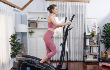 Spor ve atletik bir kadın, evdeki fiziğe ve sağlıklı spor yaşam tarzına uygun vücut egzersizi sırasında eliptik koşu makinesiyle koşuyor. Gaiety evde egzersiz eğitimi.