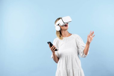 Kafkasyalı bir kız elinde telefon tutarken ve görüş açısını gösterirken VR gözlük takıyor. Görsel gerçeklik dünyasını ya da metaevreni keşfetmek isteyen mutlu kadın şaşırdı. Teknoloji yeniliği. Kısıtlanma.