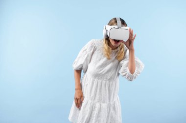 Sanal gerçeklik gözlüklü kız hologram dünyasına bakıyor. Görsel gerçeklik dünyasını kullanarak ve mavi arka planda durarak metaevreni birleştirmeye şaşıran kadın. Yenilik teknolojisi konsepti. Kısıtlanma.