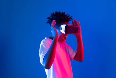 Sanal gerçekliği dijital fütüristik teknolojiye bağlayan pembe mavi neon duvarda VR 'dan bakan genç Afrikalı Amerikalı' ya şaşırdım. Entrika.