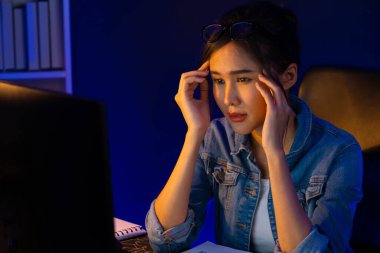 Stresli, genç, güzel Asyalı yaratıcı proje yaratıcısı sosyal medyayı araştırmak için bilgisayara bakıyor ve geceleri daha çok neon modern ofisin planlama kanalı stratejisine ulaşılıyor. Taktik.