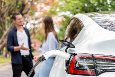 Sonbahar gezisi sırasında sonbahar ormanı EV arabasında elektrikli araba için şarj olan sevimli genç çift. Sonbahar tatilinde çevre dostu seyahat. Yükselt