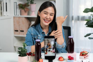 Gülümseyen, güzel Asyalı genç, lezzetli karışık çilek ve kiraz suyu detoksu içeceklerini inceleyen, sosyal medyada özel promosyon satışı için sağlıklı ürünler sergileyen. Taktik.