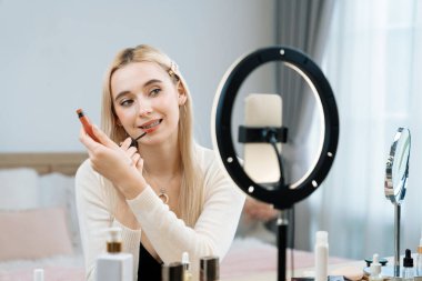 Sosyal medya için güzellik ve kozmetik video içeriği hazırlayan genç bir kadın. Seyirciye veya takipçiye nasıl sıvı ruj sürüleceğini gösterirken kamera ve ışık halkası kullanan bir güzellik blogcusu. Blithe