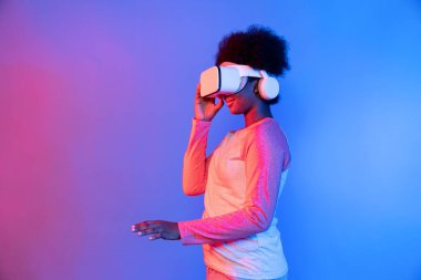 Genç Afrikalı, teknolojik dijital yenilik grafiğinde mavi neon aydınlatma grafiğinde izole edilmiş 3 boyutlu hologram veri uygulamasını seçmek için metaevren üzerinden VR gözlük takıyor. Entrika.