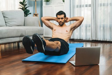 Atletik ve sporcu adam spor paspası üzerinde çatırdarken evdeki formda fiziğe ve sağlıklı spor yaşam tarzına uygun online ev eğitimi takip ediyor. Çevrimiçi neşeli ev egzersizi videosu.