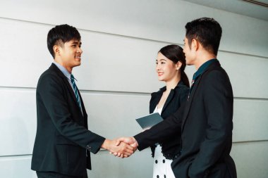 İş adamları konsepti kabul ediyor. İş adamı toplantı odasında başka bir iş adamıyla tokalaşıyor. Genç Asyalı sekreter bayan onların yanında duruyor. uds