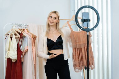 Genç sosyal medyum kadın moda videosu yapıyor. Blogcu kameraya ve ışık çemberine gülümserken, aynı zamanda ikna edici çevrimiçi kıyafetleri izleyicilere veya takipçilere vlog sattırıyor. Blithe