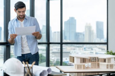 Mimari ekipman, belge, taslak ev modeli ile ev modelini karşılaştırırken, uzman inşaat mühendisi elinde plan tutuyor. Emlak tasarımı konsepti. İzleme.