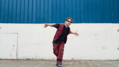 Beyaz arka planda break dans pratiği yapan yakışıklı bir sokak dansçısı. Hip hop tarzı giyinen sporcu, mavi arka planlı bir sokakta müzik eşliğinde ayak sesleri çıkarıyor. Açık hava sporu 2024. ÇalışmaComment.
