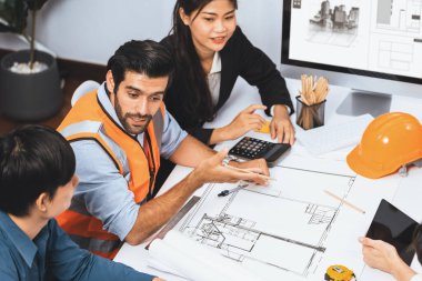 Mimari proje üzerinde birlikte çalışan çeşitli inşaat mühendisi ve müvekkil grupları, inşaat planını gözden geçirip toplantı masasında plan oluşturuyorlar. Tedbirli