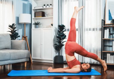 Spor kıyafetleri içinde esnek ve becerikli bir kadın evde egzersiz paspası üzerinde meditasyon pozisyonunda yoga yapıyor. Huzurlu ve huzurlu bir yoga yaşam tarzı..