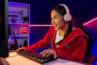 İnternet üzerinden kulaklık takıp gülümseyen Asyalı güzel kız flamasının sunucu kanalı izleyicilerle internet üzerinden konuşma yapıyor. Esport yetenekli takım oyuncuları neon mavi odada. Taktik.