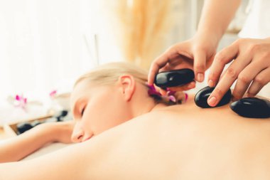 Lüks tatil köyündeki kaplıcalarda sıcak taş masajı. Gün ışığı sükunet ortamında, mutlu kadın müşteri bazalt taş masajından zevk alıyor. Rahatlatıcı bir sıcaklıkla vücudun üzerinde süzülüyor. Sessiz.