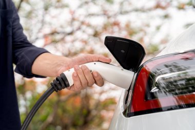 Sonbahar gezisi sırasında sonbahar ormanı arabasında elektrikli araba için şarj eden bir adam. Sonbahar tatilinde elektrikli araçla çevre dostu bir seyahat. Yükselt