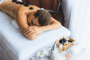 Lüks tatil köyündeki kaplıcalarda sıcak taş masajı. Gün ışığı sükunet ortamında, mutlu kadın müşteri bazalt taş masajından zevk alıyor. Rahatlatıcı bir sıcaklıkla vücudun üzerinde süzülüyor. Sessiz.