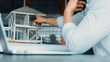 Kabiliyetli beyaz mimar el yapımı ev tasarımını dizüstü bilgisayardaki model ve plan ile karşılaştırın. Dizüstü bilgisayar kullanan profesyonel proje yöneticisi. Eline odaklan. Yönlendirici.