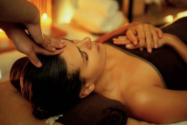 Beyaz kadın stres önleyici kafa masajı yapmaktan ve lüks otel veya otelde sıcak mum ışığında yüz güzelliği eğlencesi yapmaktan zevk alıyor. Sessiz.