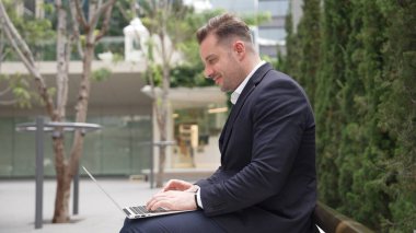 Green City 'de otururken bilgisayarla çalışan iş adamlarının yan görüntüsü. Akıllı yönetici bilgisayar yazma raporunu ve pazarlama stratejisini uzaktan kumandayla iş ekibiyle çalışırken kullanıyor. Urbane.