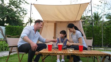 Aile hep birlikte bahçedeki kampta oturup yemek yiyor. Sevimli ebeveynler, genç nesil arasında iletişim kurmak ve zaman geçirmek için açık hava kamp faaliyetlerini kullanırlar. Uyumsuzluk.