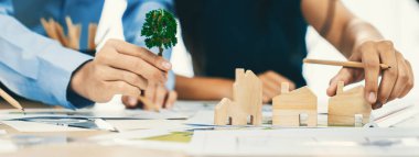 Profesyonel mimar mühendis takımı toplantı masasında ahşap blokla ve etrafa saçılmış planlarla mimari projeyle ilgili tartışır. Tasarım ve işbirliği konsepti. - Yakın çekim. Tanımlama.