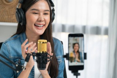 Asyalı sunucu canlı yayında canlı yayında canlı yayında sosyal medyada kulaklık takarak konuşuyor. Dinleyicileri modern stüdyoda koçluk yaparak selamlıyor. Taktik.