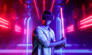 Lazer kılıcı tutan ve VR gözlük takan oyuncu. Beyaz adam, neon şatonun etrafında dikilirken görsel gerçeklik kulaklığı kullanıyor. Yenilik teknolojisi. Sapma.