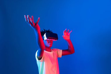 Genç Afrikalı Amerikalı basketbol oyuncusu, metaevren dünyasında dijital fütüristik teknolojiyi birbirine bağlayan mavi neon ışıkta zıplayan VR pozu takıyor. Entrika.