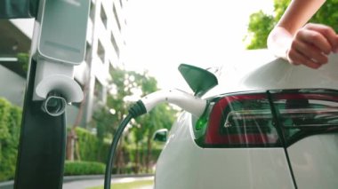 Yavaş çekim çift yazın yeşil sürdürülebilir şehir açık bahçesinde elektrikli araba şarj ile seyahat elektrikli aracın temiz yeniden şarj edilebilir enerjisi için kentsel sürdürülebilirlik yaşam tarzı olarak