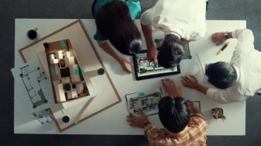 Mimar mühendis ekibinin tartıştığı ve tablet görüntüleme inşaatını planlı ve ev modeliyle toplantı masasında işaret ettiği en tepeden aşağı bakış açısı. Çeşitli tasarımcı tasarım evleri. Hizalama.