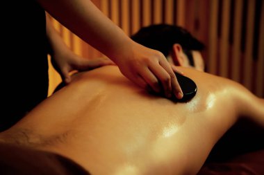 Sıcak mum ışığıyla lüks bir tatil köyündeki kaplıca salonunda sıcak taş masajı, mutlu erkek müşteri bazalt taşı masajının keyfini çıkarırken rahatlatıcı bir sıcaklıkla vücudun üzerinde süzülüyor. Sessiz.