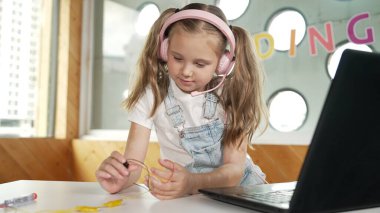 Elektronik ekipman çalışırken kulaklık takan güzel bir kız. Laptop, tornavida ve kablolar masanın yanına yerleştirilirken beyaz çocuk fen deneyleri yapıyor. Akıllı online sınıf. Etkinlik.