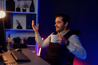 Gülümseyen zeki işadamı, elinde kahve fincanı olan satış ekibiyle buluşuyor ve geceleri Mor Neon Light Home Office 'deki bilgisayar ekranında ürün hedef pazarını araştırıyor. Tahmin et..