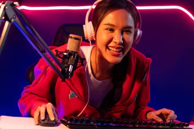 İnternet üzerinden kulaklık takıp gülümseyen Asyalı güzel kız flamasının sunucu kanalı izleyicilerle internet üzerinden konuşma yapıyor. Esport yetenekli takım oyuncuları neon mavi odada. Taktik.