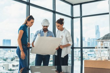 Bir grup mimar mühendis proje planına bakarken, yapı hakkında beyin fırtınası yapıyorlar. İdari ekip inşaat hakkında şehir manzaralı bir yerde dururken tartışıyor. İzleme.